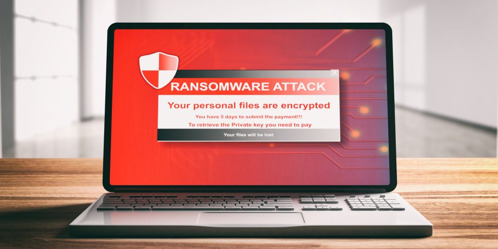 Ransomware attack on a computer laptop screen, wooden desk. 3d illustration | Schools Week