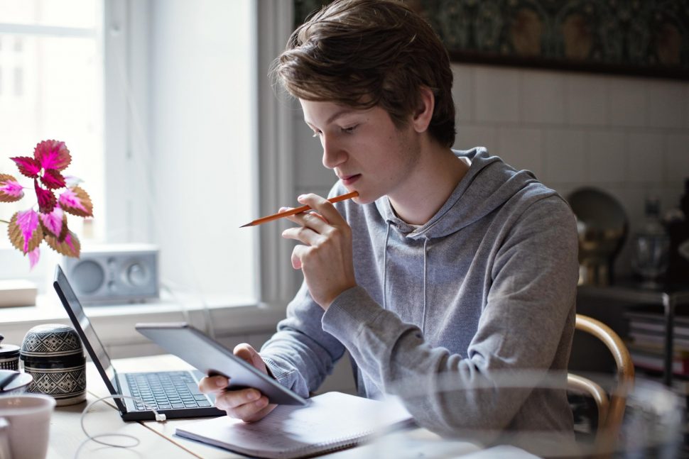 Koncentrerad tonårskille använder läsplatta under läxläsning hemma | Schools Week